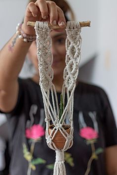 a woman holding up a plant in a pot with ropes attached to it's sides