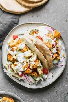 two tacos are sitting on a plate next to some pita bread and other food