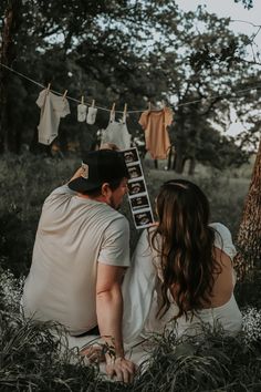 a man and woman sitting next to each other in the grass with clothes hanging on a line