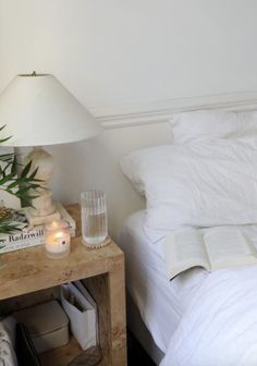 a bed with white sheets and pillows next to a table with two candles on it