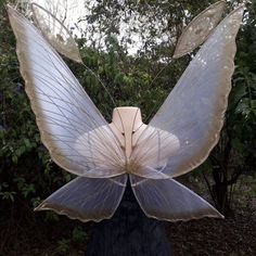 a sculpture of a butterfly with wings spread out in front of some bushes and trees