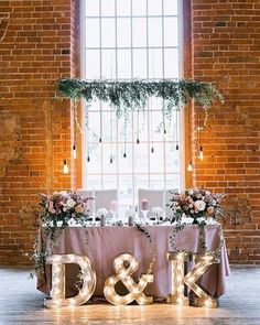 the letters are lit up in front of a table with flowers and greenery on it