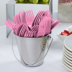 a bucket full of pink forks sitting on top of a table next to plates and grapes