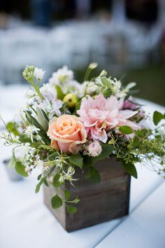 a wooden box filled with flowers on top of a white table cloth covered tablecloth