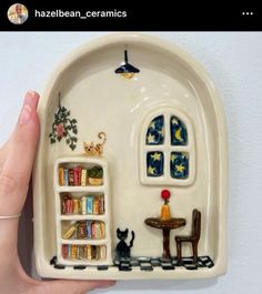 a hand is holding a ceramic plate with a miniature house on it and bookshelves in the shape of a book shelf