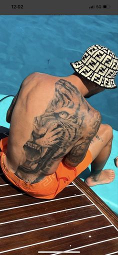 a man sitting on top of a blue surfboard next to a swimming pool with a tiger tattoo on his back