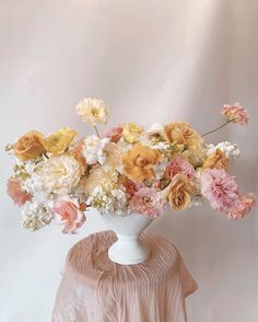 a white vase filled with lots of flowers on top of a pink tablecloth covered table