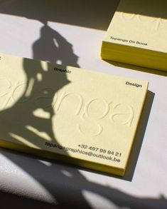 two yellow business cards sitting on top of a white table with shadows from the person's shadow