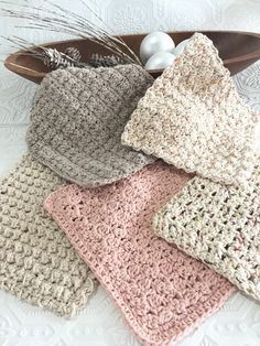 four crocheted dishcloths in various colors on a wooden tray next to an egg