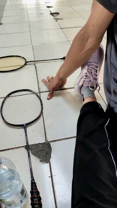 a person standing on a tiled floor with tennis rackets and water bottles next to them