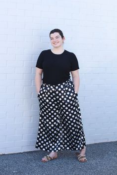 a woman standing in front of a white brick wall wearing black and white polka dot pants