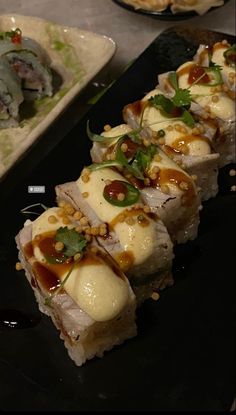 sushi is served on a black plate with garnishes and sauces