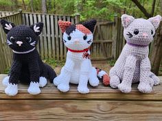 three crocheted cats sitting next to each other on a wooden table in front of a fence