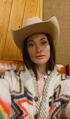 a woman wearing a cowboy hat sitting on top of a brown leather chair next to a wooden wall