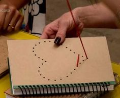 two people working on an art project at a table with notebooks and pencils