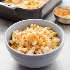 a bowl filled with macaroni and cheese next to a pan of breadcrumbs