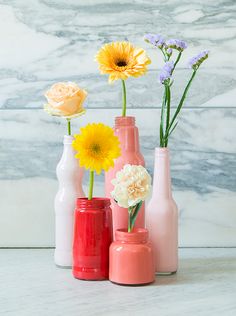 three vases with flowers in them on a table next to a marble wall background