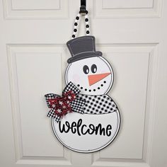 a welcome snowman door hanger hanging on a white door with black and red checkered ribbon