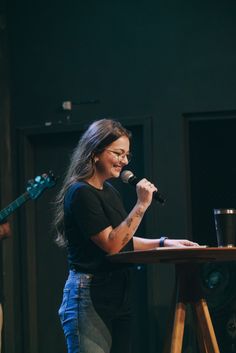 a woman standing at a table with a microphone in her hand and singing into a mic