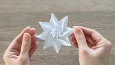 two hands holding an origami star on top of a wooden table next to each other