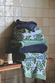 stack of folded towels sitting on top of a wooden table next to a tiled wall