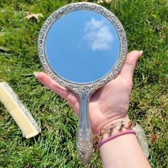 a person's hand holding a mirror with a blue sky in the reflection and a comb of grass next to it