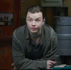 a man sitting at a table with his hands on his chest and looking into the camera