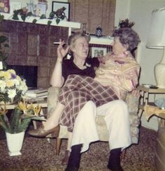 an old photo of two women sitting in a living room with flowers on the table