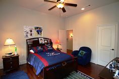 a bed room with a neatly made bed next to a blue chair and a ceiling fan