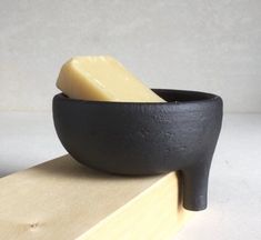 a black bowl with a piece of cheese in it sitting on top of a wooden block