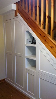 an open book shelf under the stairs in a room with white walls and wood floors