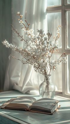 an open book sitting on top of a table next to a vase filled with flowers