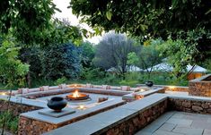 an outdoor fire pit surrounded by stone walls and benches with lit candles in the middle