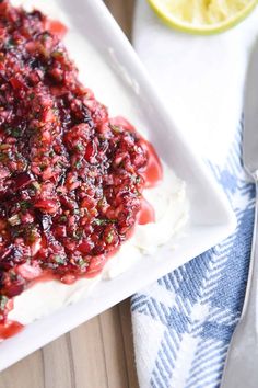 a white plate topped with cake covered in cranberry sauce next to a lemon wedge