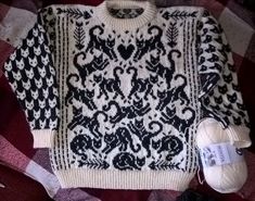 a white and black sweater sitting on top of a plaid blanket next to yarn balls