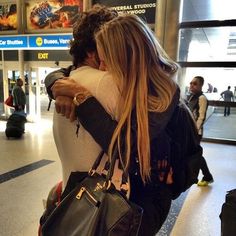 two women hug each other in an airport terminal as they wait for their luggage to arrive