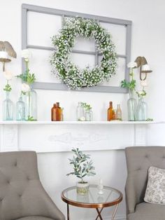 two chairs and a table in front of a fireplace with wreaths on the mantle