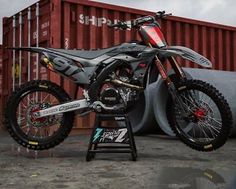 a dirt bike sitting on top of a metal stand next to a shipping container in the background