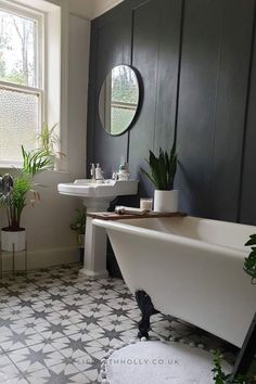 a white bath tub sitting next to a sink in a bathroom under a window with potted plants