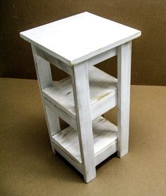 a small white wooden table with shelves on the top and bottom shelf, sitting on a brown surface