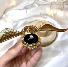 a hand holding a golden harry potters flying brooch with a black stone in it