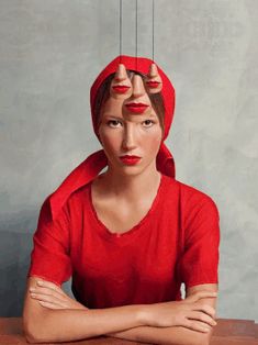 a woman sitting at a table with red lipstick on her face and hands behind her head