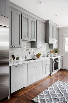 a kitchen with gray cabinets and white counter tops, wood floors, and a rug on the floor