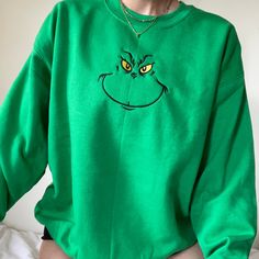 a person wearing a green sweatshirt with a grin face drawn on the front and yellow eyes