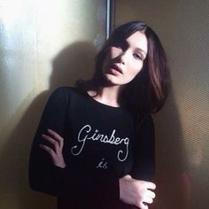 a woman standing in front of a wall wearing a black shirt with the word ginsburg is on it