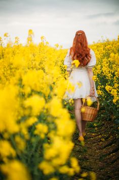 a woman with long red hair walking through a field full of yellow wildflowers