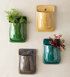 three green and yellow vases with plants in them on a white wall next to a potted plant