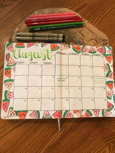 a calendar with watermelon on it sitting on a wooden table next to markers and pencils