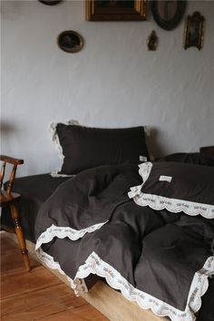 an unmade bed with black sheets and ruffles on the edges, in front of a white wall