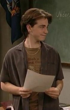 the young man is holding a piece of paper in front of a chalkboard with writing on it